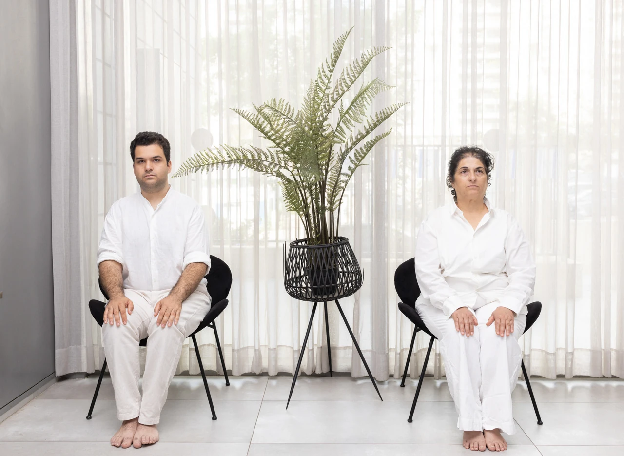 Two people in white seated apart beside a potted palm